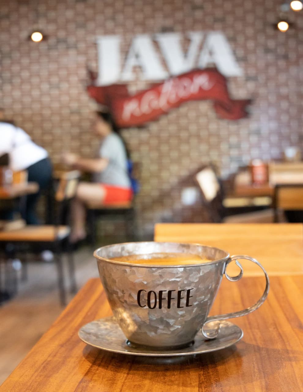 A cup of coffee on a wooden table in front of the Java Nation sign