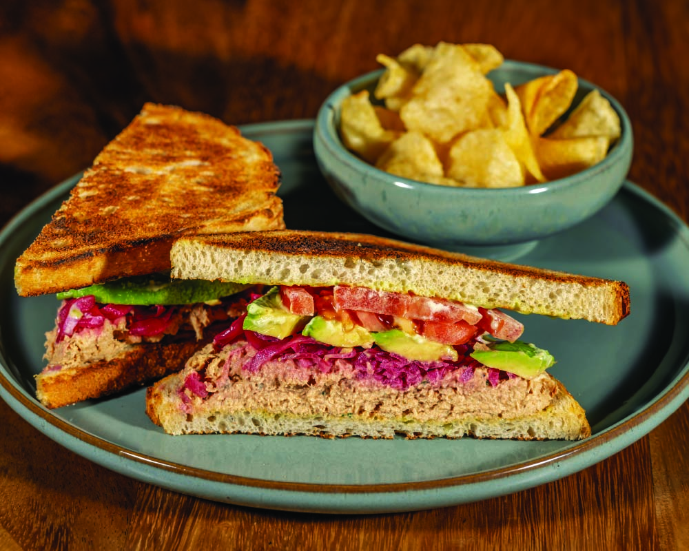 Tuna avocado sandwich on sourdough with a bowl of chips